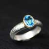 A Beautiful Handmade Ring. Sparkling Solitaire Swiss Blue Topaz Oval used in centre. The impression impression on silver is all handmade. Metal used is Sterling Silver & 18K Gold.